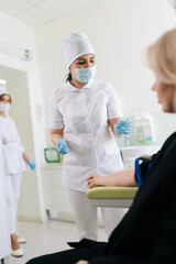 Vertical shot of woman sitting on chair talking to friendly nurse. Smiling healthcare worker taking...