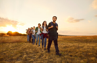 Team of tourists enjoying beauty of nature on trekking or hiking tour in countryside in autumn. Group of happy healthy male and female hikers with backpacks walking through field in morning or evening