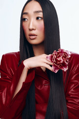 Beautiful Asian woman with long black hair in a red jacket holding a delicate flower in hand