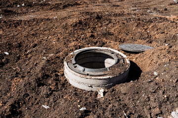 Concrete manhole cover on construction site surrounded by exposed soil and earth. Part of urban...