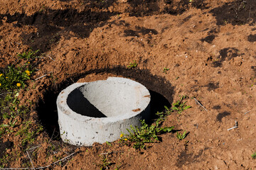 A concrete pipe section partially buried in soil, surrounded by vegetation and dry ground, in an...