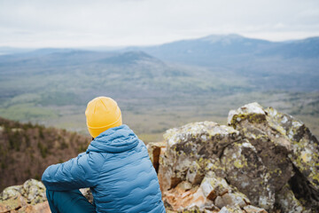 Alone in yellow beanie, person enjoys scenic view of misty mountain landscape from rocky summit on...