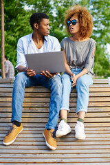 Two african american young bloggers dressed in stylish casual wear discussing app on website...