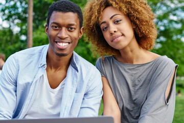 Portrait of happy couple in love with modern laptop device smiling at camera resting in urban setting.Positive african american young man with dark skinned girlfriend spending leisure time together