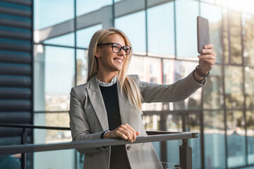 Beautiful smiling businesswoman having a video call or taking a photo while standing on the balcony...