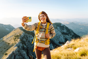 Young woman  taking selfie portrait on the top of mountain. Hiking, sport, travel and technology concept. 