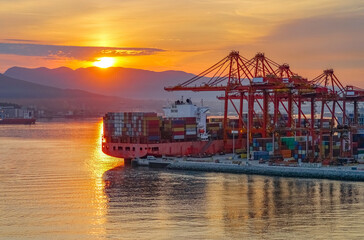 Logistics of Container Cargo ship with working crane bridge in shipyard during sunrise