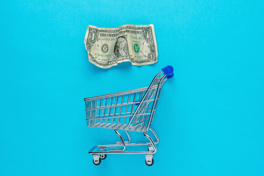 Crumpled dollar bancnote with a shopping cart on blue background. Minimal Coronavirus outbreak. Saving money concept.