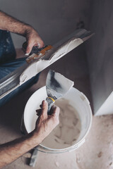 Fototapeta premium Worker puts putty on a spatula for plastering internal walls in a living room. plasterer works plastering two trowels plasterboard.