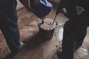 Workers put dry plaster into a bucket. Workers mixing concrete in bucket indoors. A professional...