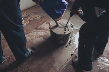 Workers put dry plaster into a bucket. Workers mixing concrete in bucket indoors. A professional...