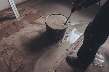Worker mixing concrete in bucket indoors. Man is mixing spackling paste putty in the bucket. Grind...
