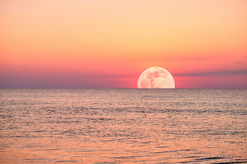 A vibrant moonlight the ocean, with a fiery sky and calm waters.