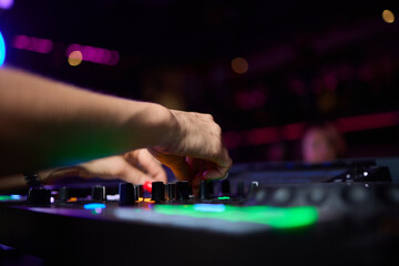 control DJ for mixing music with blurred people dancing at party in nightclub.