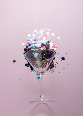 Martini glass with colorful glitters on pink background. Creative minimal party concept.