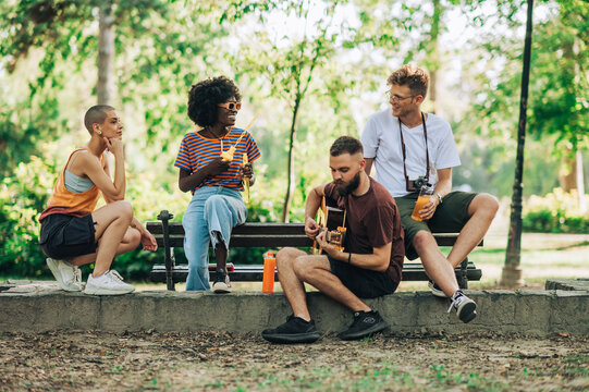 Group of multicultural hippie friends having jam session in park.