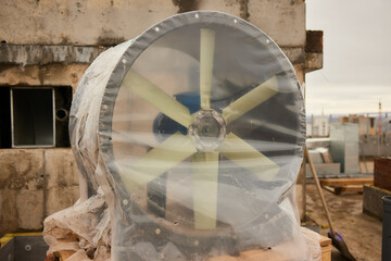 A huge fan covered in plastic sits on a rooftop against the skyline