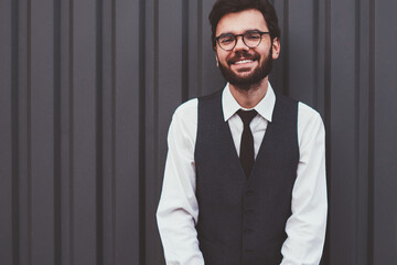 Half length portrait of successful male student looking at camera and smiling while standing near...
