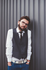 Uncertain caucasian hipster guy in spectacles standing near promotional background and looking at camera outdoors, young male student in casual wear posing near copy space area for advertising text