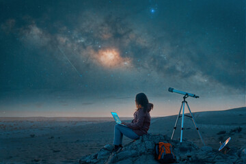 female digital nomad working with a laptop in the desert next to a telescope and satellite dish at...