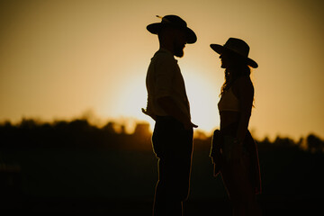 Side view and silhouette of rancher couple outdoors at sunset.