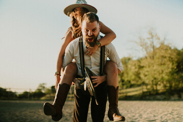 Front view of fun rancher couple having piggyback ride at homestead.