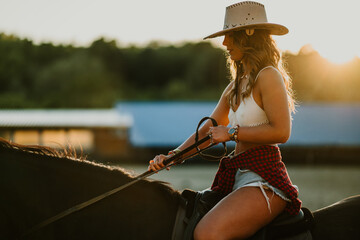 Side view of attractive rider in western outfit riding a horse at ranch