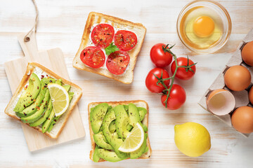 Variation of healthy breakfast toasts with avocado and cherry tomatoes on white wooden background. Food concept.