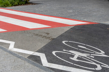 A shared space where a bicycle lane is clearly marked with a white bike symbol on tarmac, adjacent to a pedestrian crossing with red and white stripes, promoting road safety