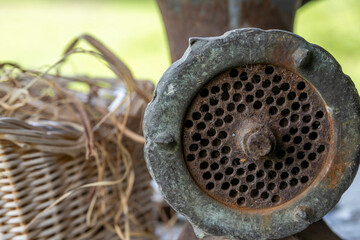 The image showcases an old, rusted metal grinder, featuring a perforated cylinder with a handle....