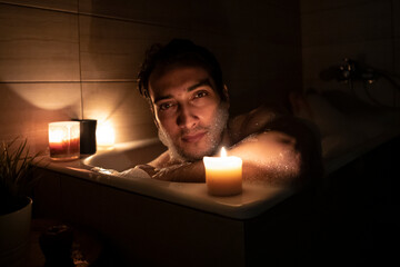 Handsome man bathing in the candlelight. Self care and spa concept	