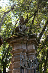 In the summer park there is an ancient stone high gate with an iron lattice, on top there is a statue of a dragon, vertical view