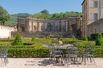 A beautiful summer park with figured trees and paths in the courtyard of an ancient villa, fenced with an ancient stone wall with sculptures, there is figured garden furniture made of metal