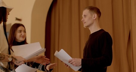 People talking indoor. Girl engages in conversation with boy while holding a paper in hands....