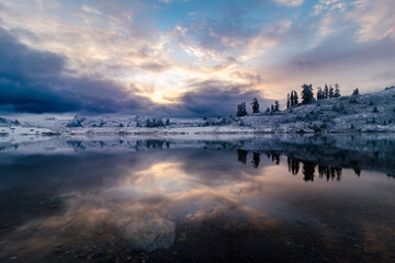 Naklejka premium Sunrise in winter next to lake and trees and mountain