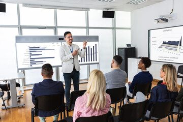 Male CEO standing in front of a multiracial group of colleagues. Multimedia classroom with smart board and graphics on them.