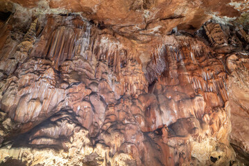 A cave with a lot of brown and white rock formations. The rock formations are very large and the...