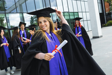 Portrait of graduate student standing in front of her friends with toga and diploma all happy.