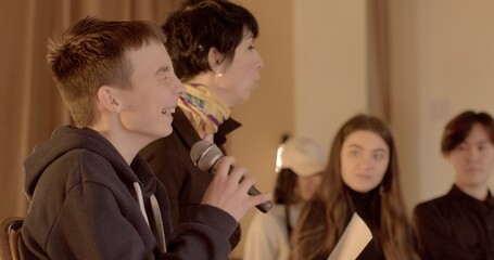 The teacher facilitator listens to the microphone. Warm cozy indoors. Teenage student speaks during school debate, High school students listen attentively and nod positively. 