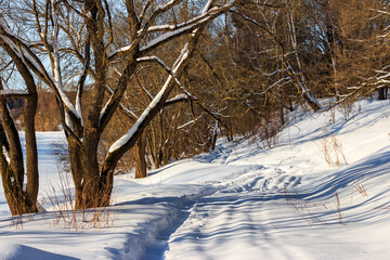 Path along a snowy slope near a river in winter, winter landscape with a sunny day