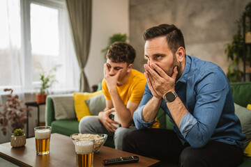 Two man friends are disappointed while watch football match at home
