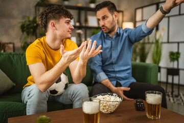 Two man friends are disappointed while watch football match at home