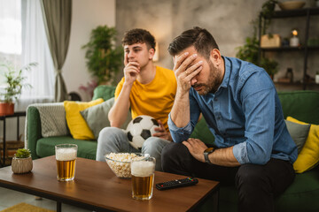 Two man friends are disappointed while watch football match at home