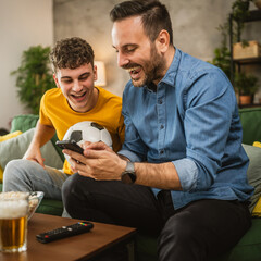 Two male friends follow football match results on mobile phone at home