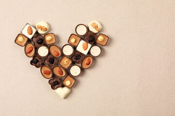 Heart made with delicious chocolate candies on beige background, top view. Space for text