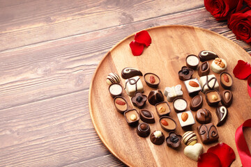 Heart made with delicious chocolate candies and rose petals on wooden table. Space for text