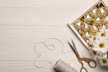 Delicious heart shaped chocolate candies, scissors and twine on white wooden table, flat lay. Space for text