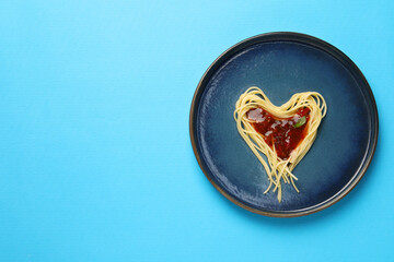 Heart made with spaghetti and sauce on light blue background, top view. Space for text