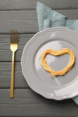 Heart made with spaghetti and fork on grey wooden table, top view