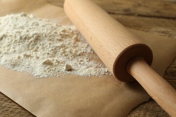 Parchment with flour and rolling pin on wooden table, closeup